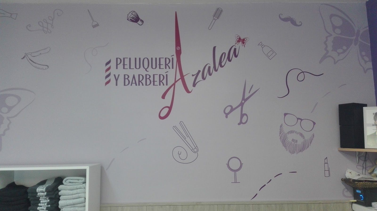 Pared lila del salón con el logo de Peluquería y Barbería Azalea, tijeras, mariposas y dibujos de peluquería